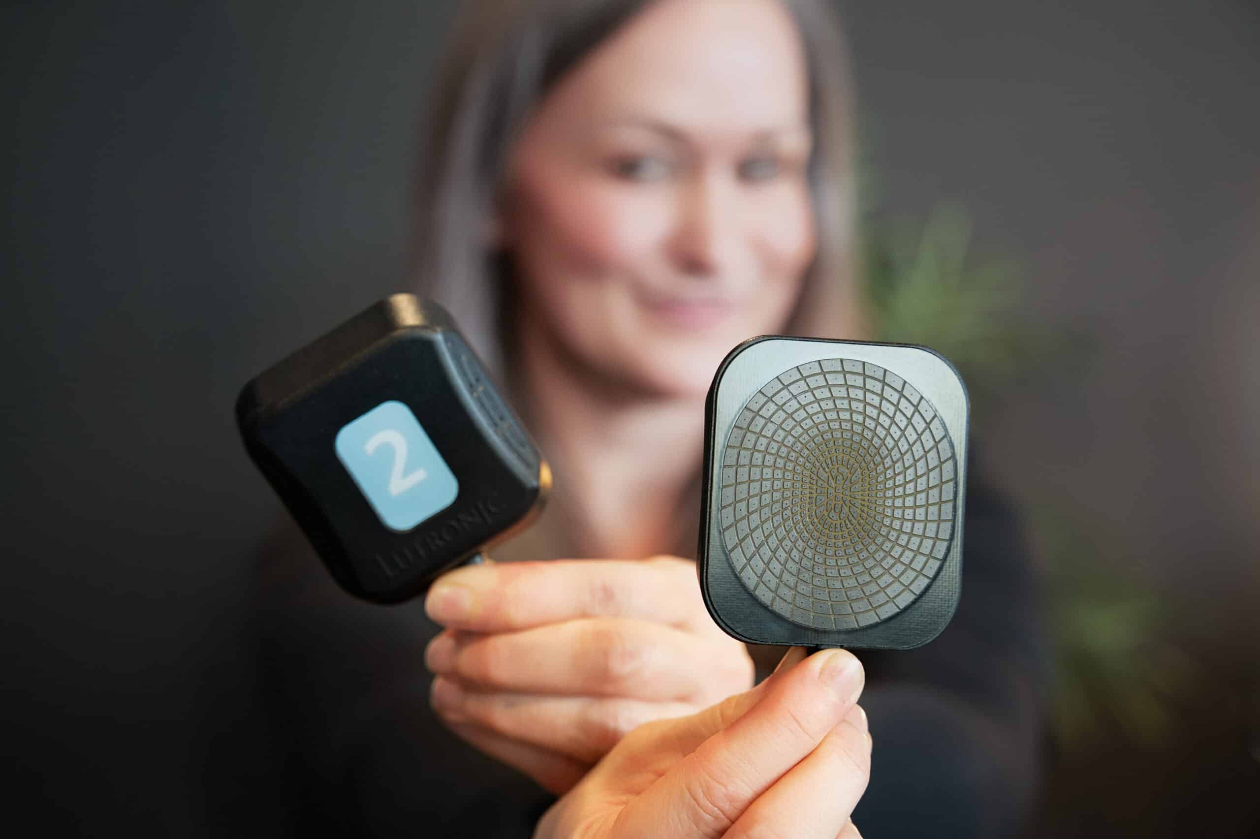 Accufit body sculpting device held in foreground with person blurred in background at RevitalyzeMD.